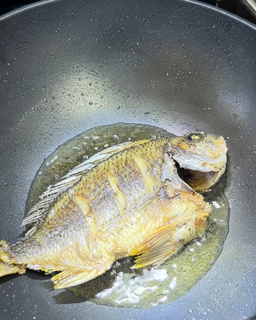 Ingwerscheiben und Knoblauch verstreut um den gebratenen Fisch in einem Wok.