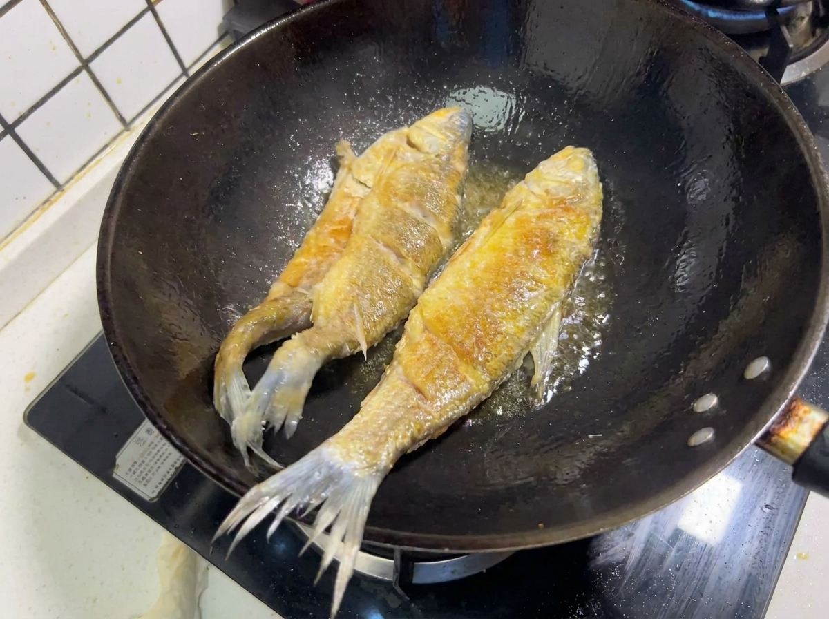 Zwei ganze Fische braten in heißem Öl in einem Wok und zeigen eine knusprige, goldbraune Kruste.