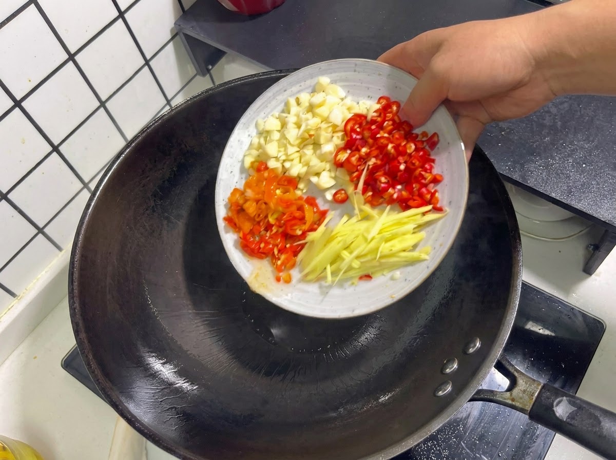 Gehackter Knoblauch, rote Chilischoten, eingelegte Paprikaschoten und Ingwerstreifen werden in einen Wok gegeben.