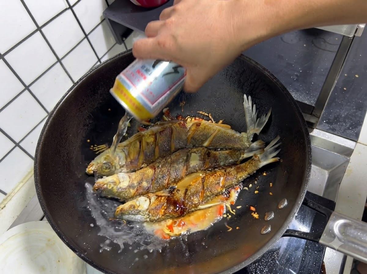 Eine Hand gießt eine Dose Bier in einen Wok über den gewürzten frittierten Fisch und die sautierten Aromen.