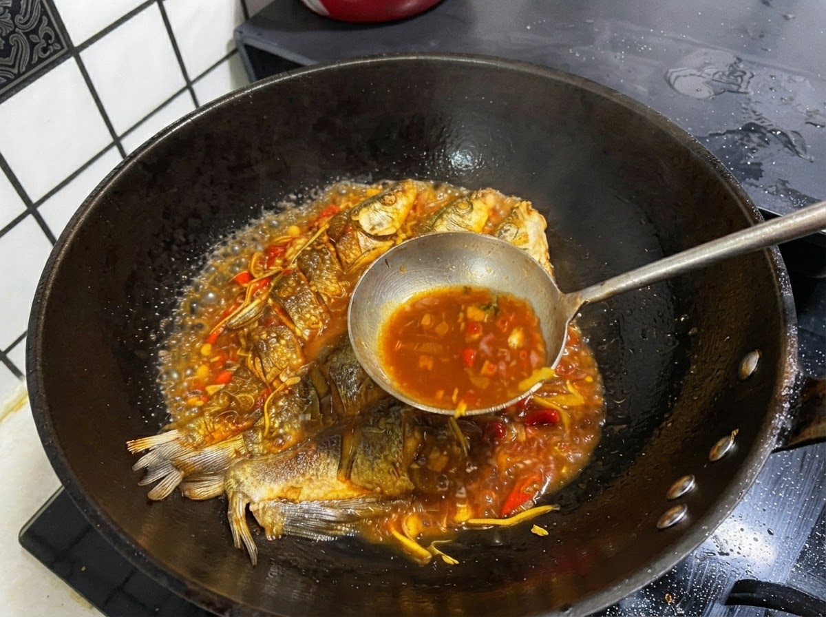 Eine Metallkelle schöpft dunkle, herzhafte Brühe aus einer Pfanne mit ganzen frittierten Fischen.