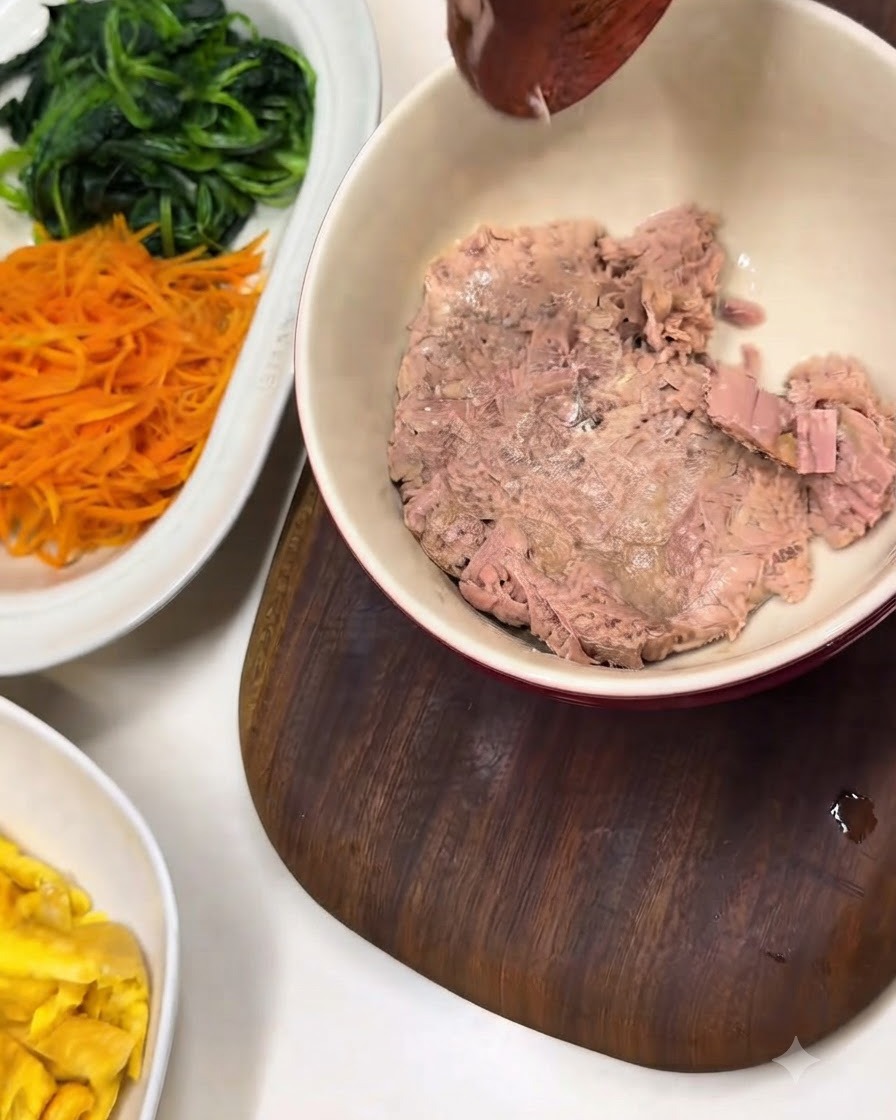 Eine Schüssel mit Thunfischflocken neben einer weißen Platte mit vorbereitetem Spinat und Karotten.
