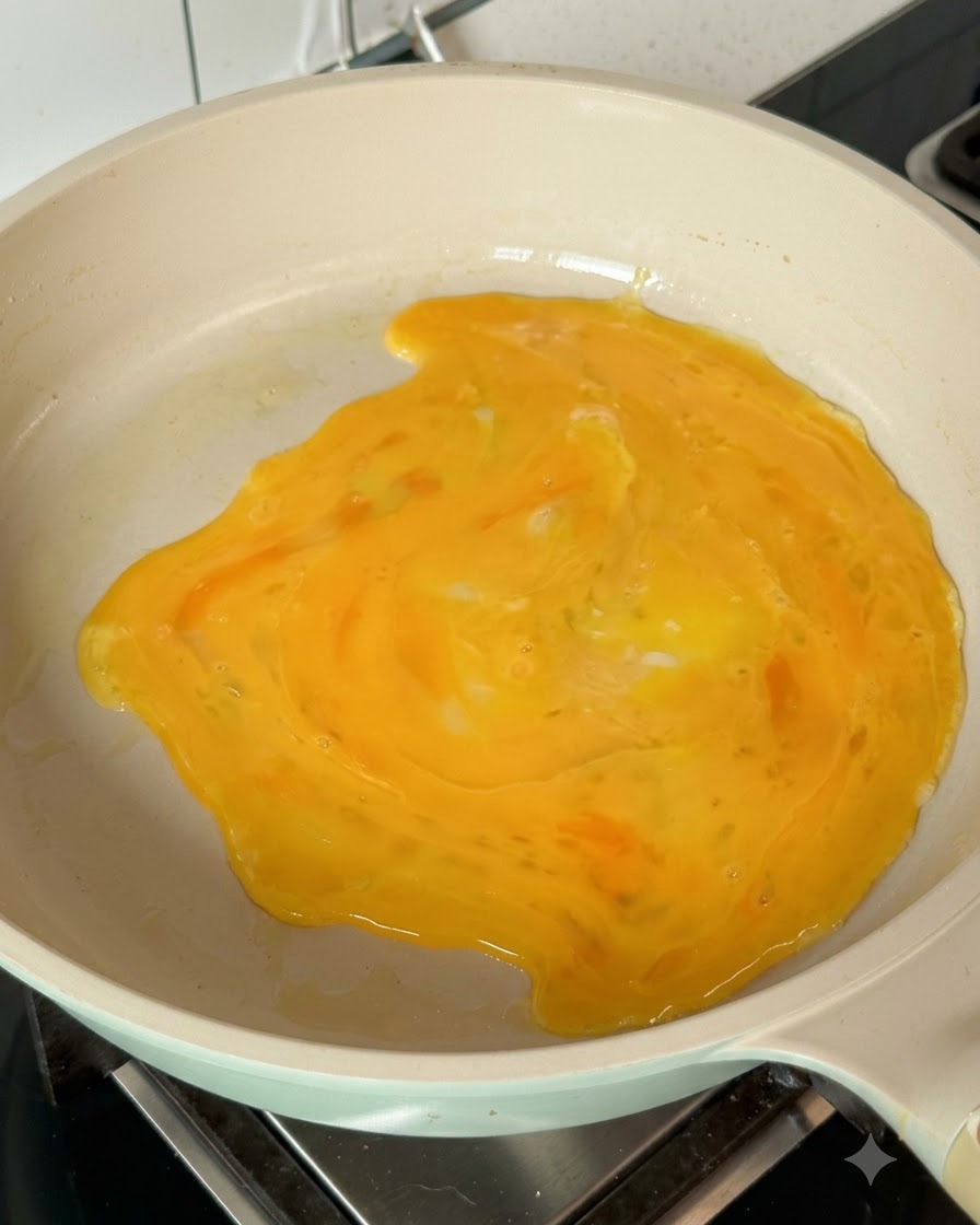 Verquirlte Eier verteilen sich in der heißen Pfanne und bilden einen Eierpfannkuchen.
