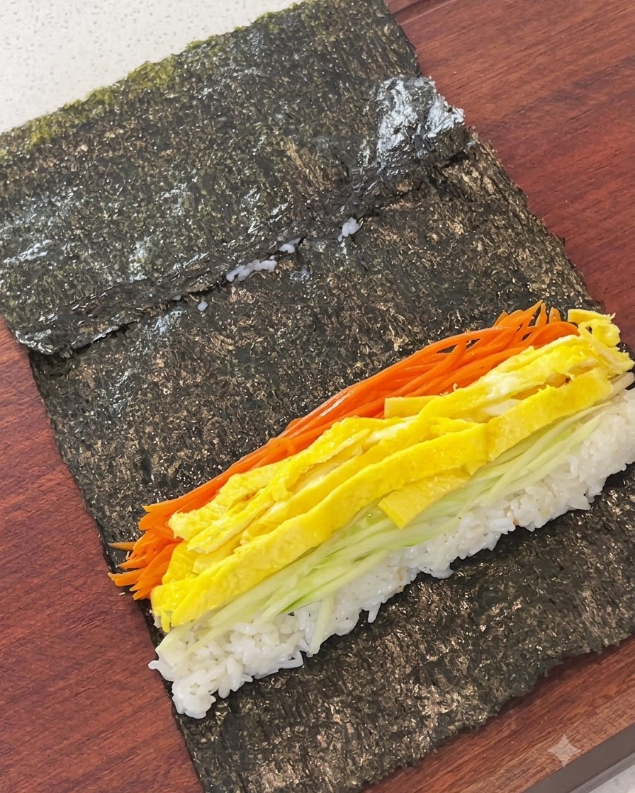 Geraspelte Karotten, Eierstreifen, Gurke und Fischkuchen auf Reis auf einem Algenblatt angeordnet.