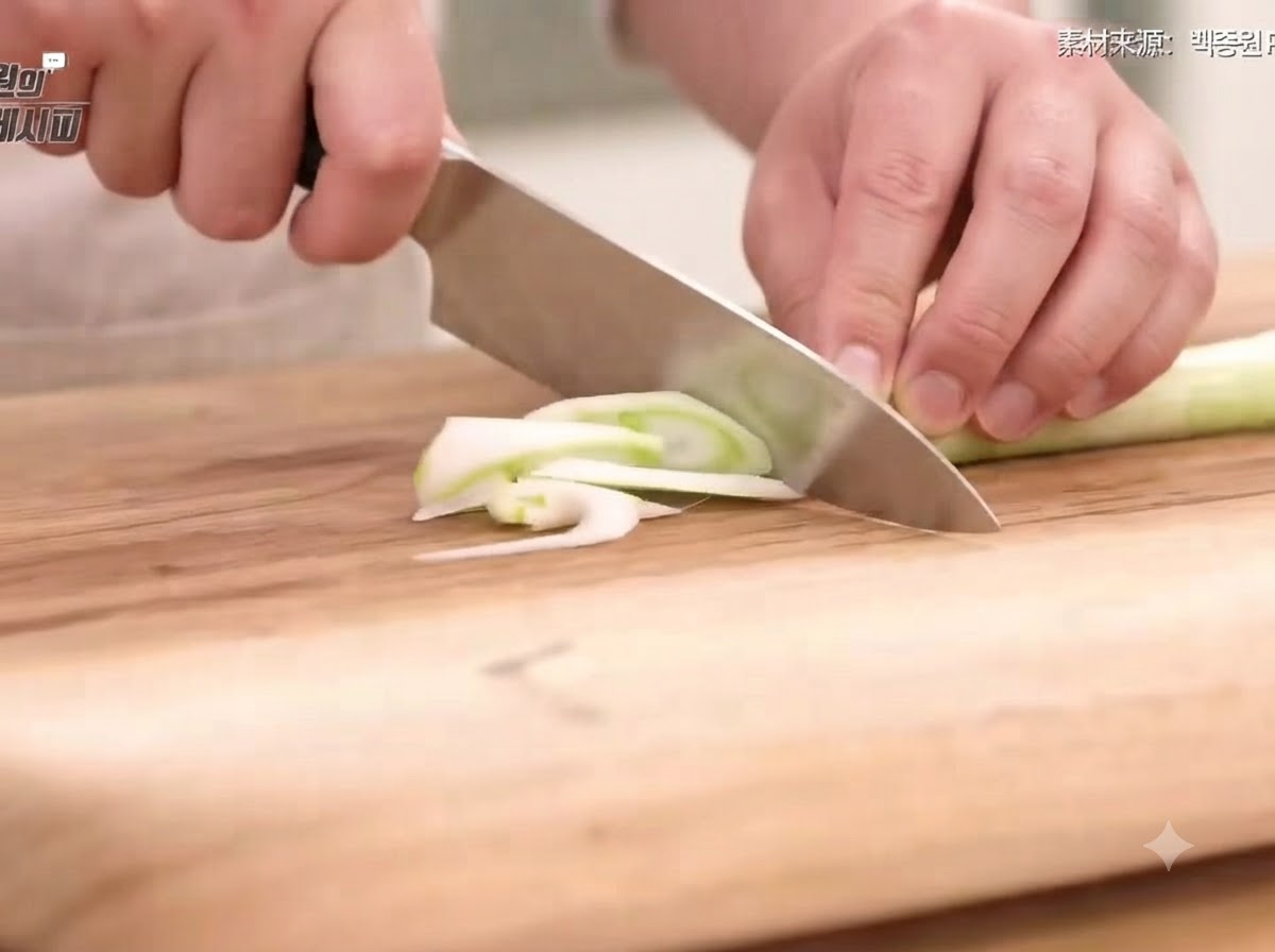 Frühlingszwiebel, Zwiebel, Karotte und Chilischoten werden auf einem Holzschneidebrett mit einem Messer in dünne Scheiben und Streifen geschnitten.