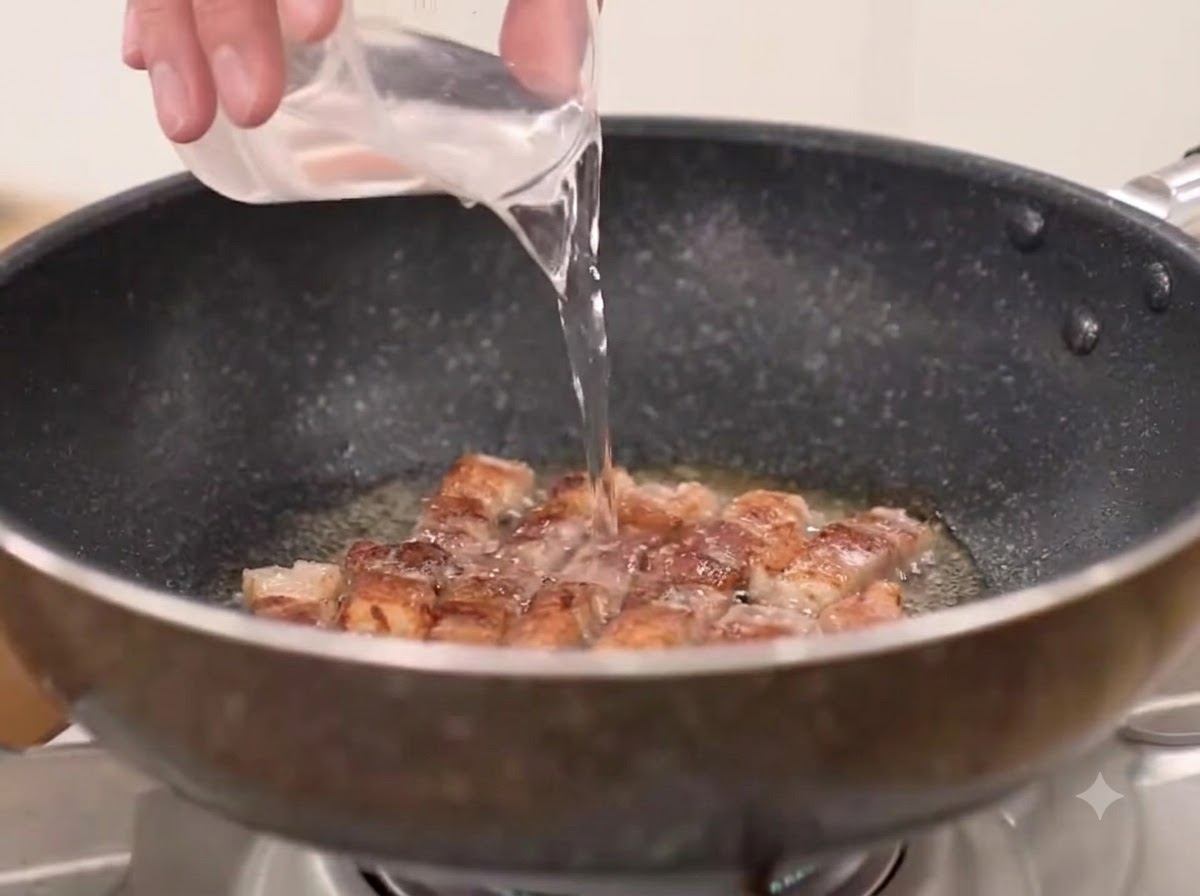 Wasser, grobes Chilipulver und Kimchi werden in die Pfanne zum angebratenen Schweinebauch gegeben.