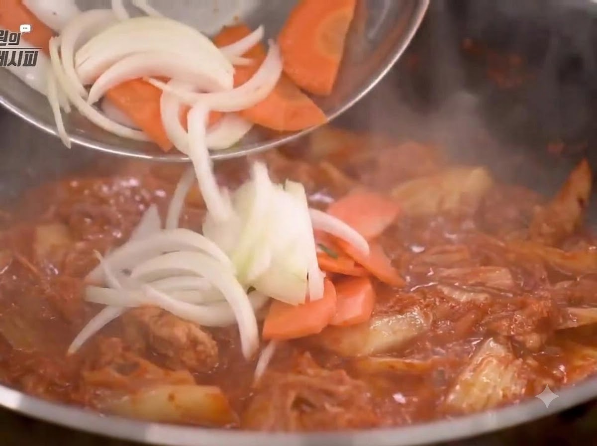 Geschnittene Zwiebeln und Karotten werden in die Pfanne gegeben und mit der Kimchi-Mischung angebraten.