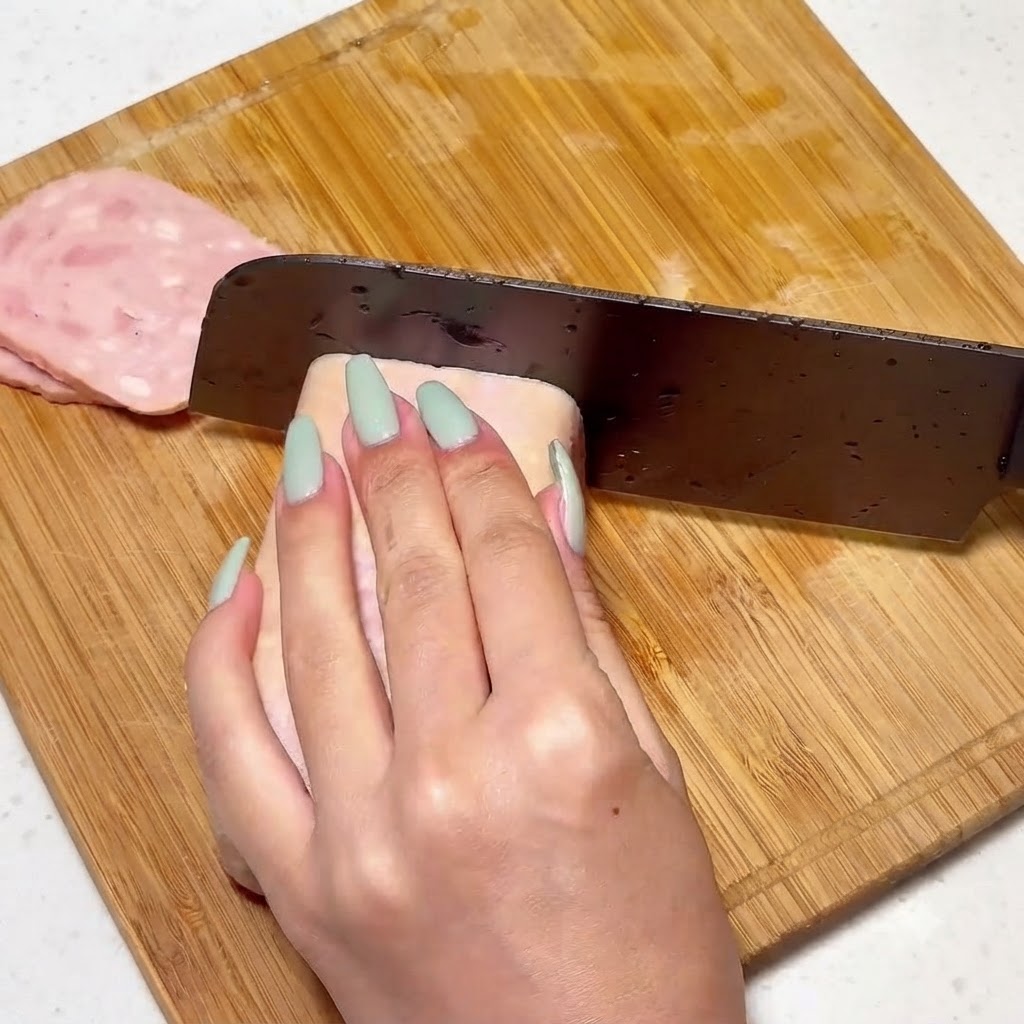 Frühstücksfleisch wird auf einem Holzbrett mit einem Messer gleichmäßig in Scheiben geschnitten.