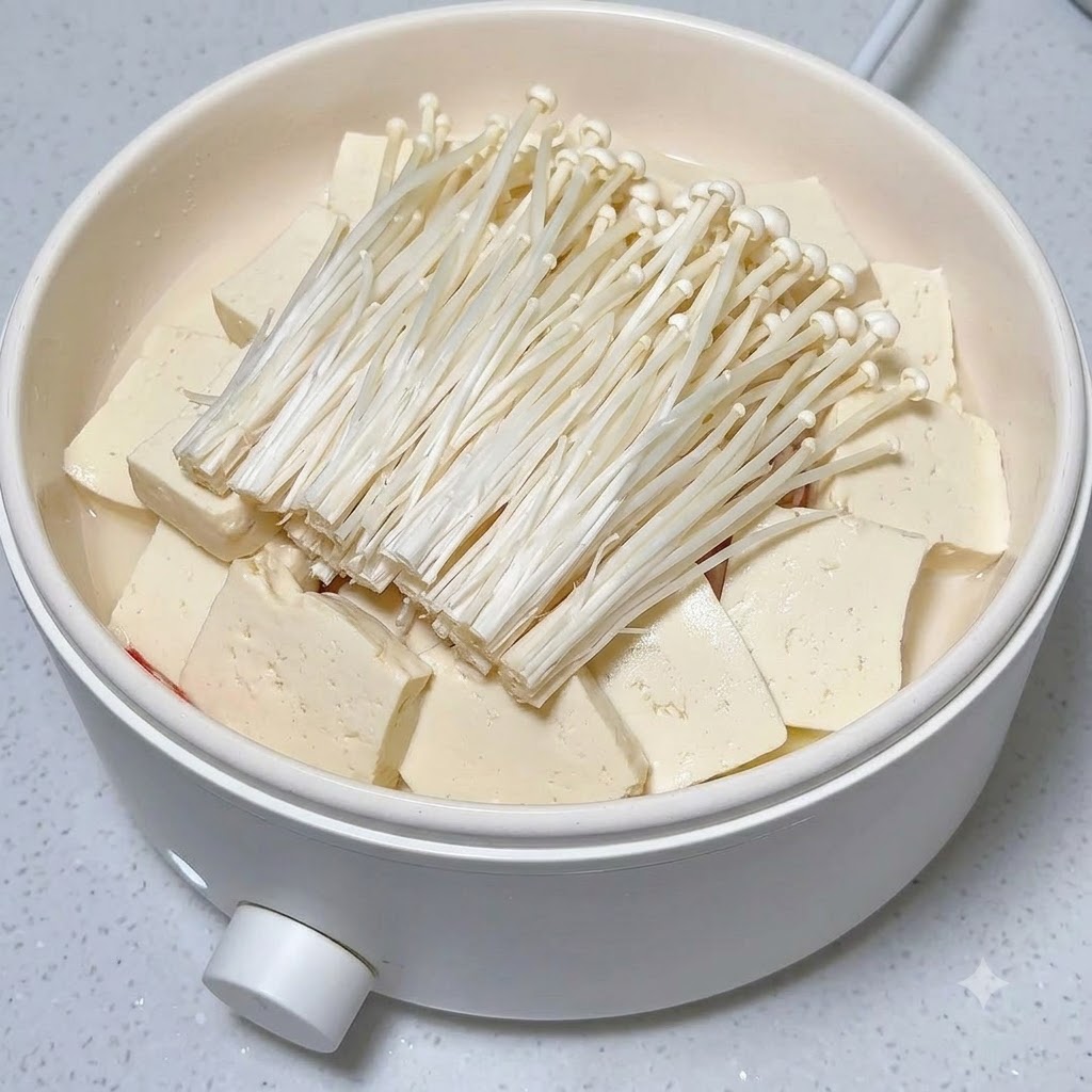 Frische rote Chilischeiben sind ordentlich auf einem Haufen Enoki-Pilze und Tofu in einem weißen Topf angeordnet.