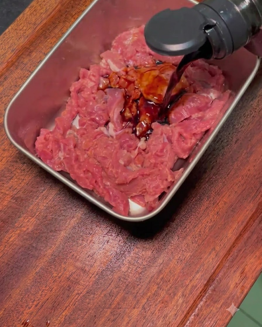 Dunkle Marinade wird in einem rechteckigen Metalltablett über rohes, in Scheiben geschnittenes Rindfleisch gegossen.