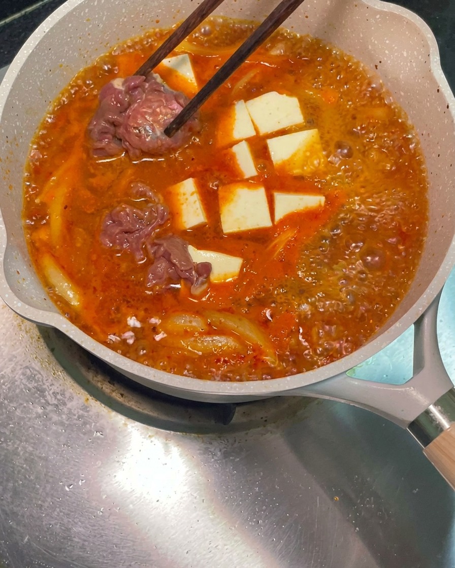 Essstäbchen platzieren rohe, marinierte Rindfleischscheiben in der simmernden roten Suppenpfanne.