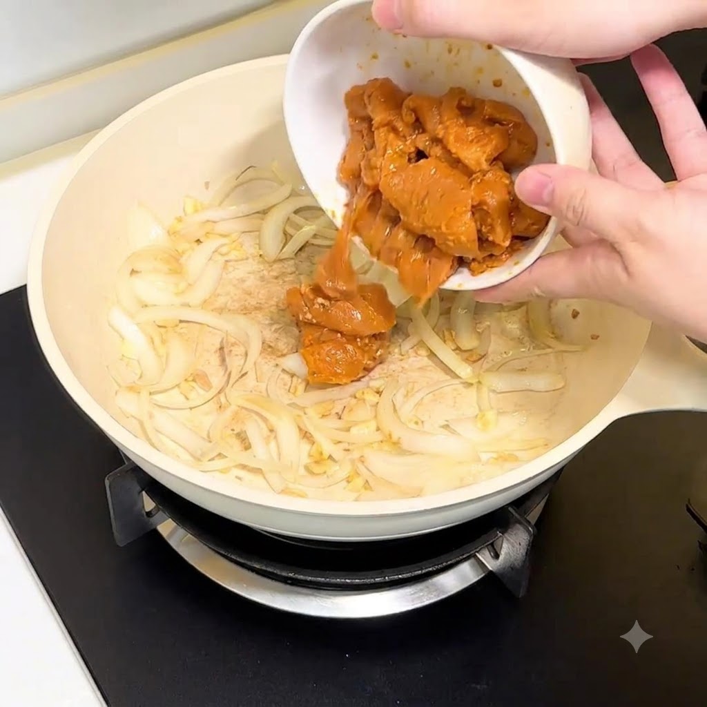 Hähnchenbruststücke werden aus einer weißen Schüssel in die Pfanne mit Zwiebeln und Knoblauch gegeben.