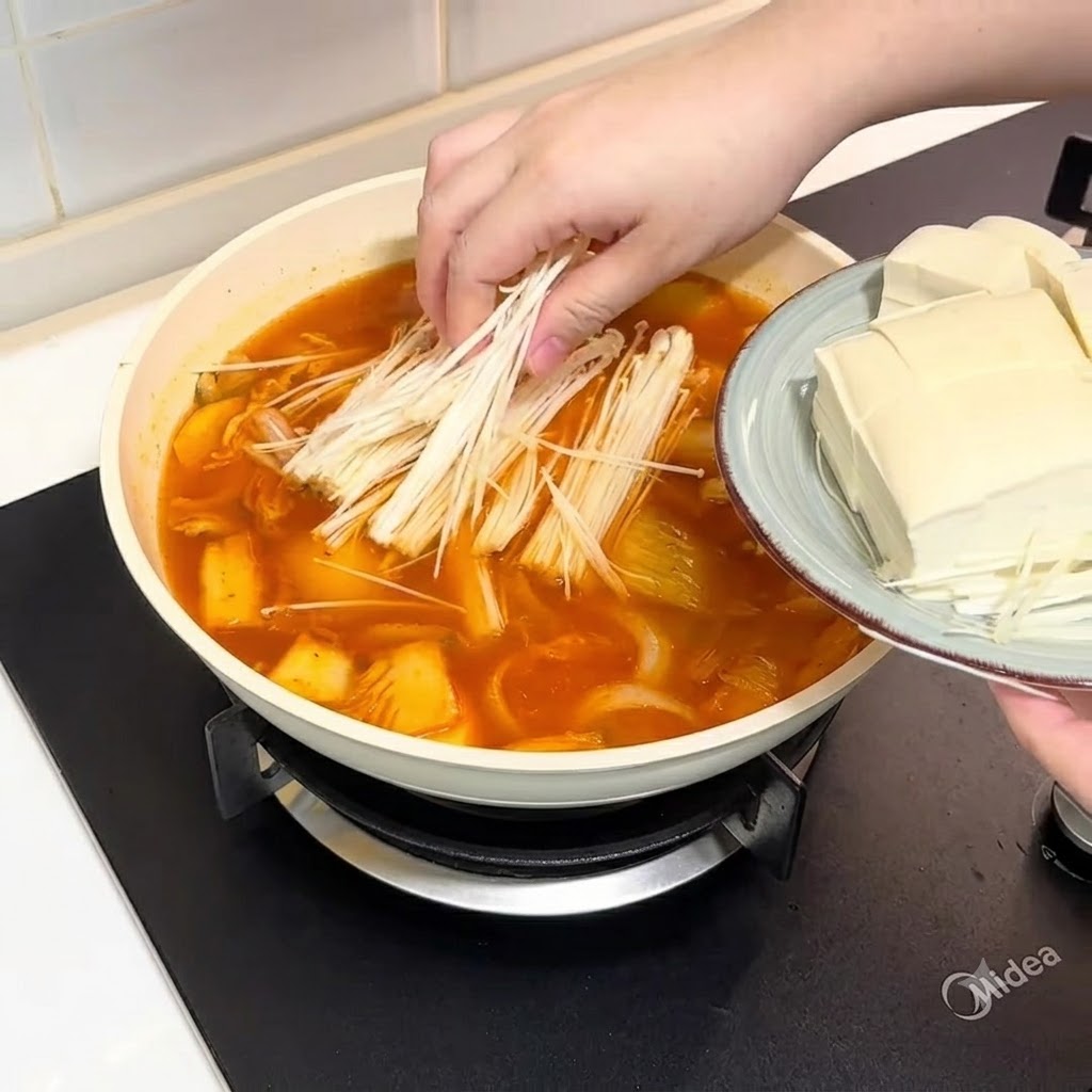 Enoki-Pilze und geschnittener Tofu werden in den Topf mit Brühe gegeben.