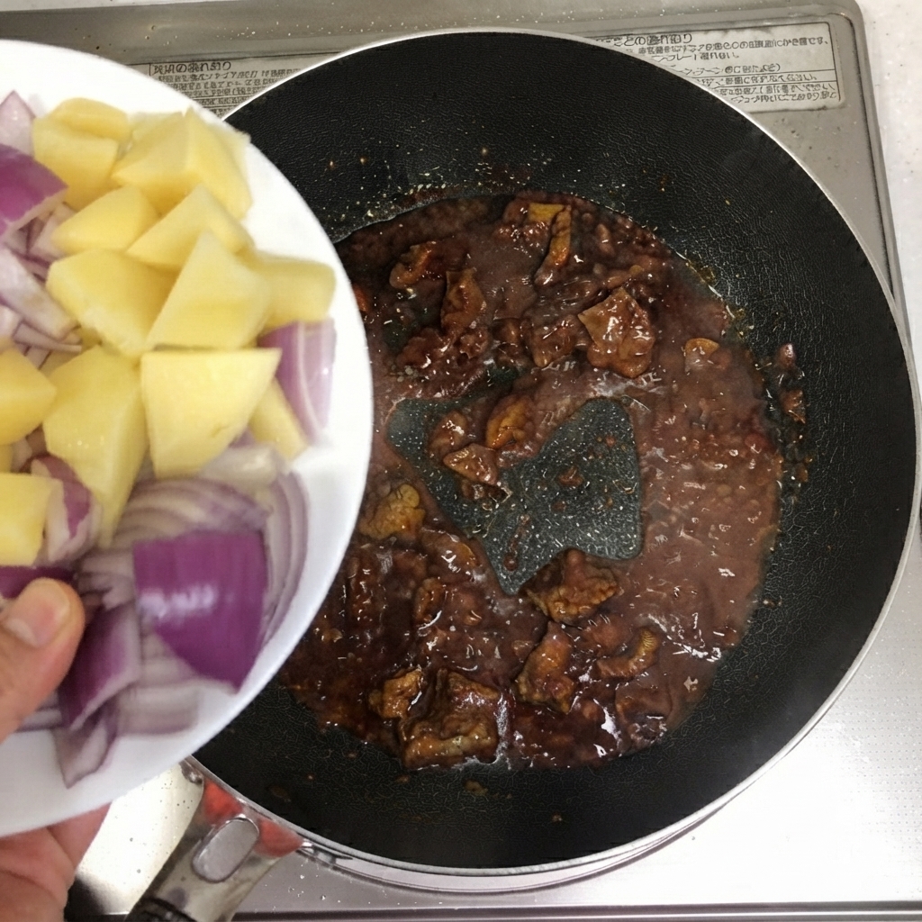 Geschnittene Kartoffeln und rote Zwiebeln werden von einem Teller in die Pfanne mit Rindfleisch gegeben.