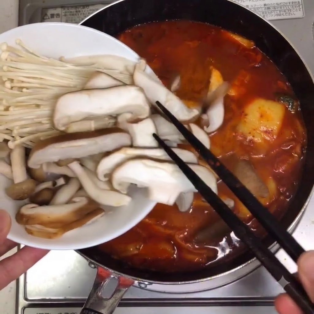 Gemischte Pilze und Enoki-Pilze werden mit Staebchen in den koechelnden Suppentopf gegeben.