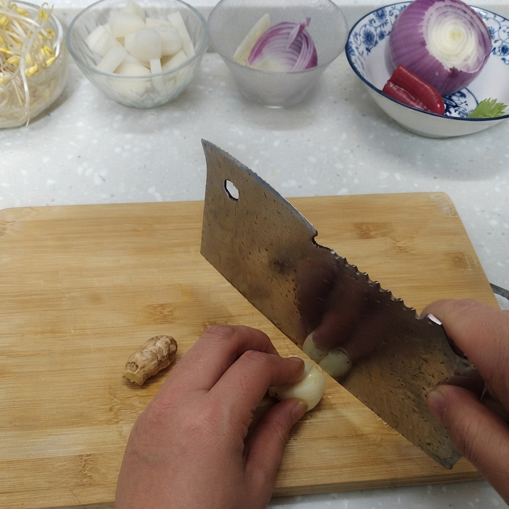 Knoblauchzehen und frischer Ingwerspross werden neben Schüsseln mit Zutaten auf einem Schneidebrett geschnitten.