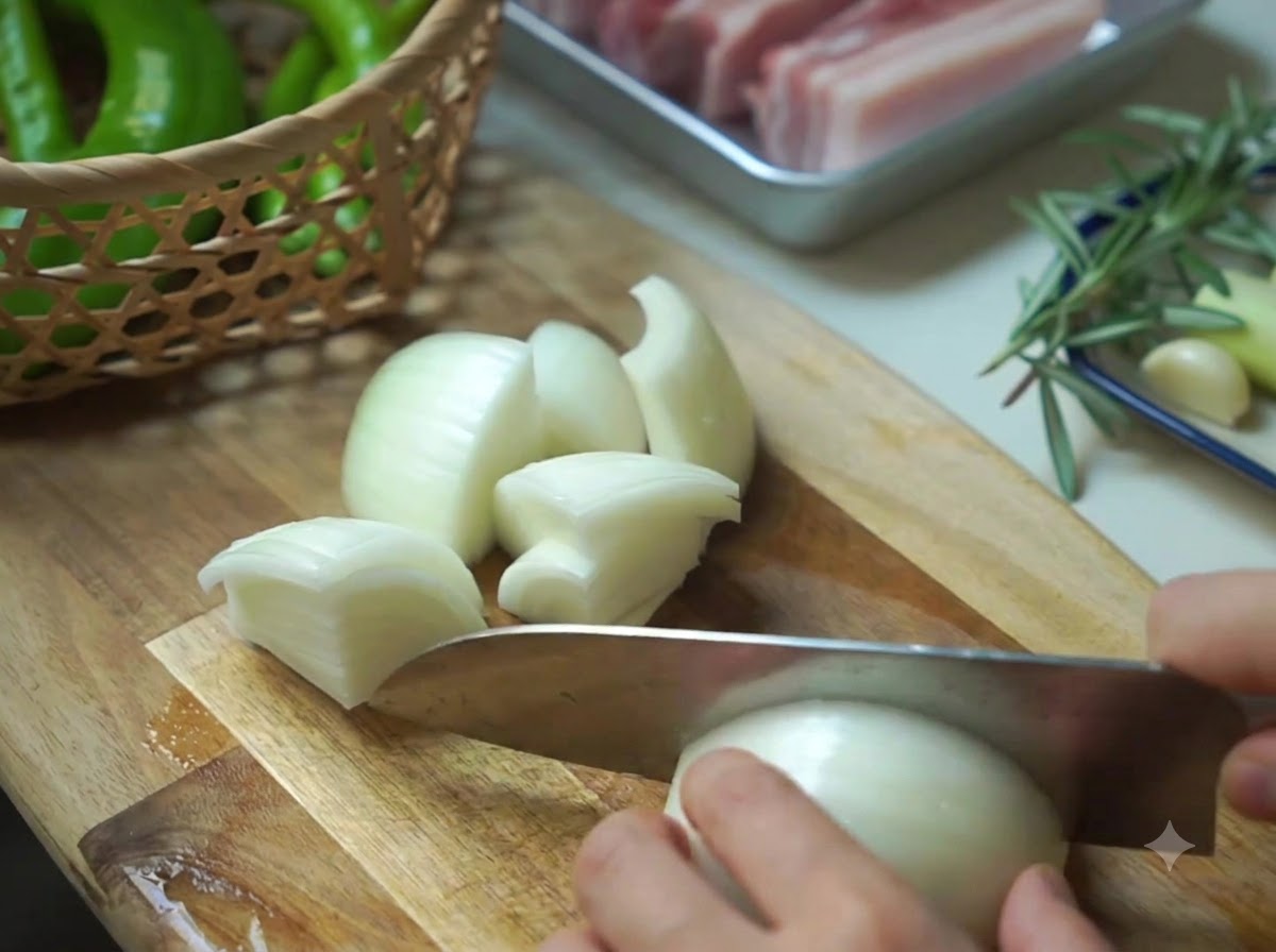 Eine Zwiebel wird neben einem Korb mit grünen Peperoni auf einem Holzbrett in Stücke geschnitten.