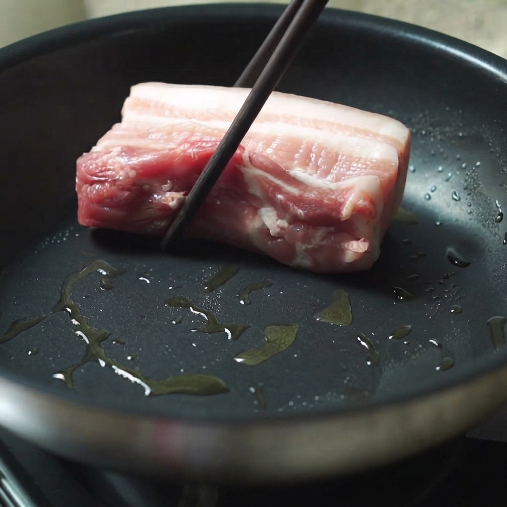 Ein dickes Stück Schweinebauch wird mit Stäbchen in eine heiße, eingeölte Bratpfanne gelegt.