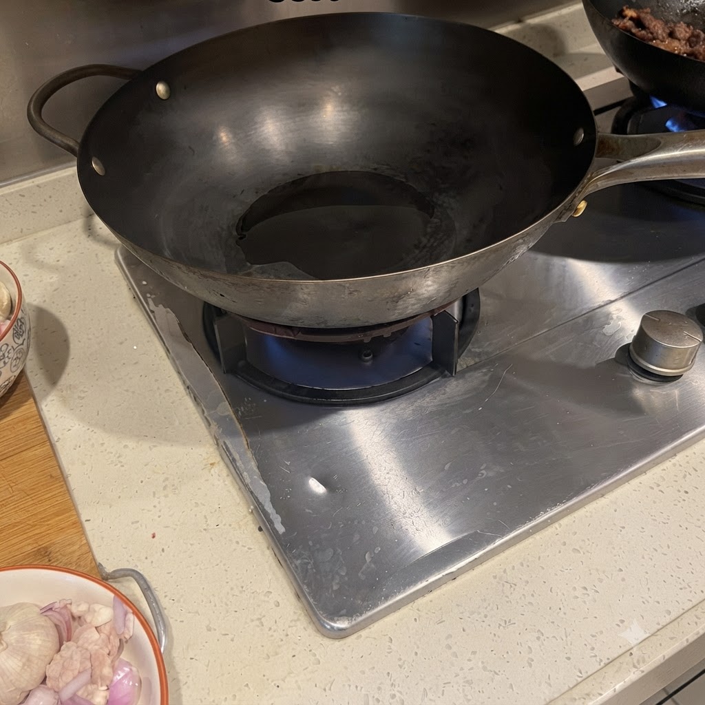 Schweinebauch und rote Zwiebel brutzeln in einem heißen Wok mit Öl.