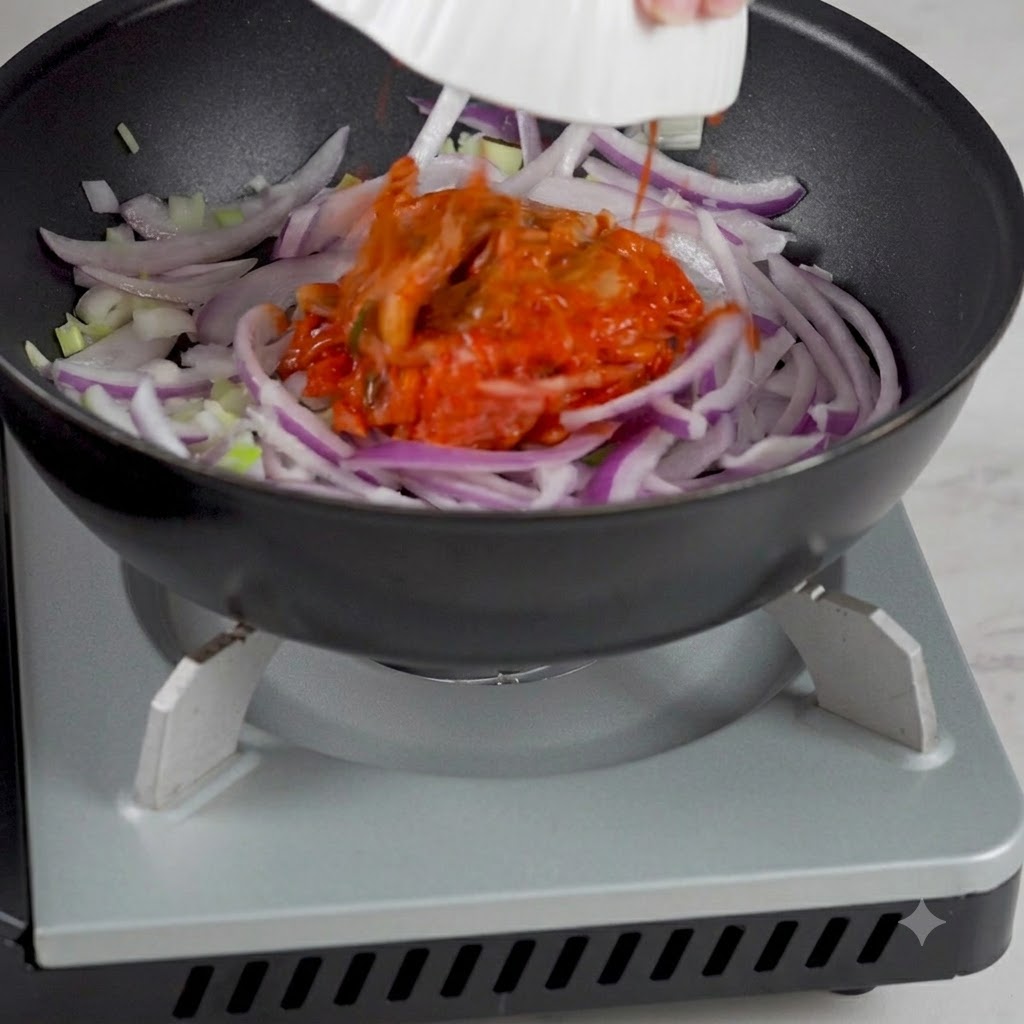 Koreanisches Kimchi wird aus einer Schüssel in die Pfanne mit den angebratenen Zwiebeln gegeben.