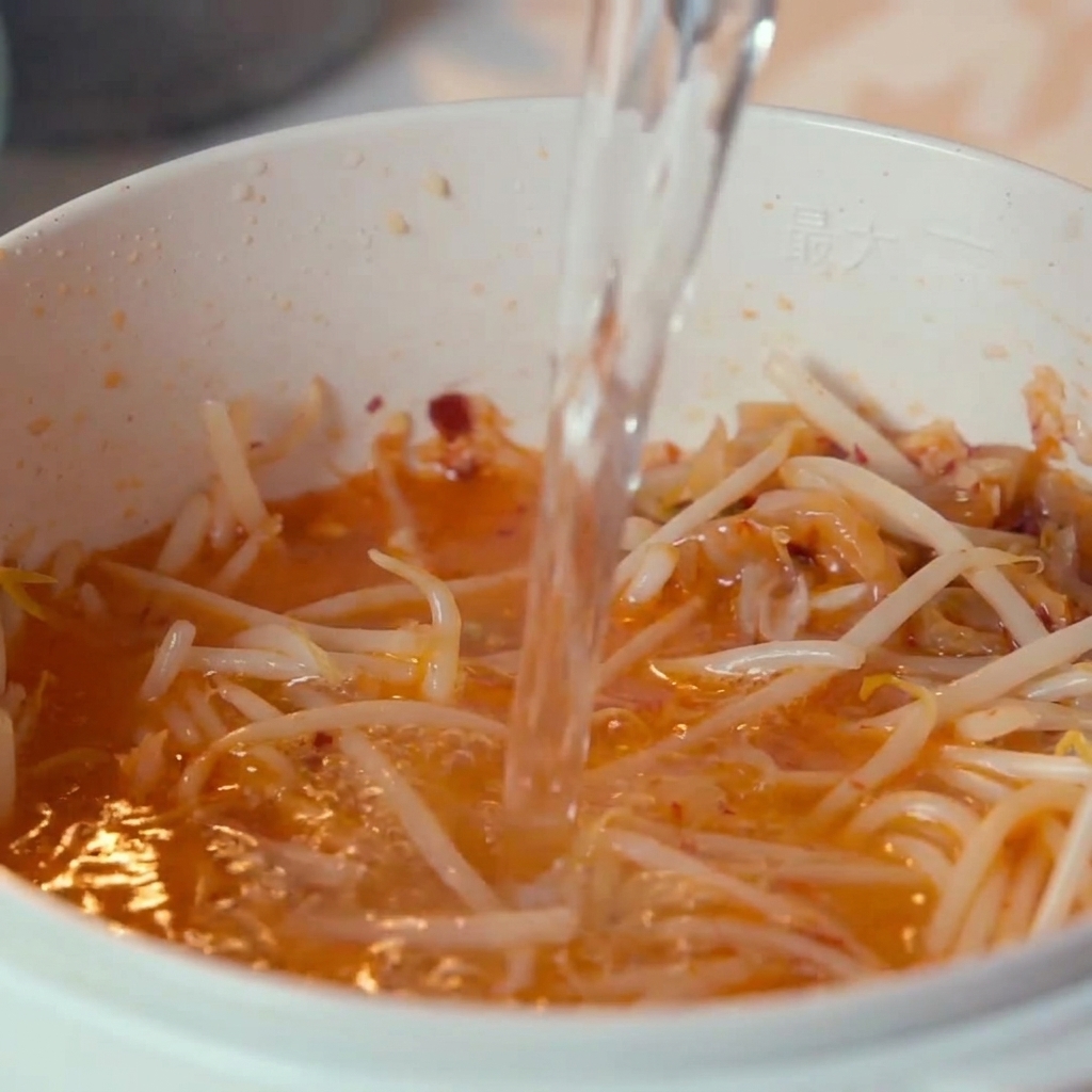 Wasser wird von oben in den Topf mit Kimchi und Sojasprossen gegossen.