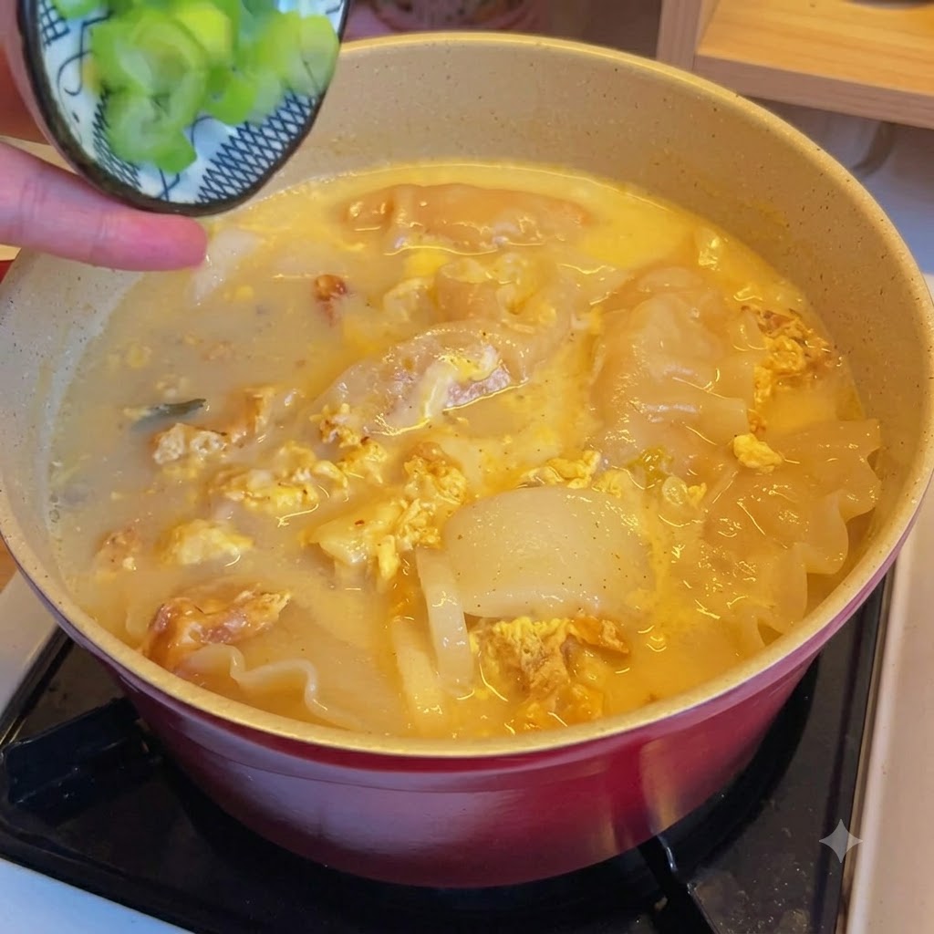 Gehackte Frühlingszwiebeln werden über einen Topf mit Kimchi-Teigtaschen-Suppe gestreut.