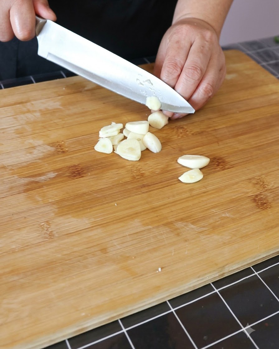 Knoblauchzehen werden auf einem Holzschneidebrett fein gehackt.