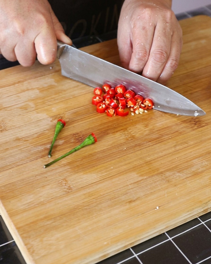 Frische rote Thai-Chilischoten werden auf einem Holzschneidebrett in kleine Ringe geschnitten.