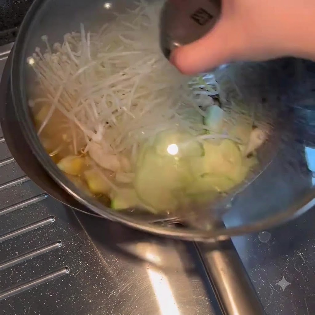 Ein Glasdeckel wird auf eine mit köchelndem Gemüse und Brühe gefüllte Bratpfanne gelegt.