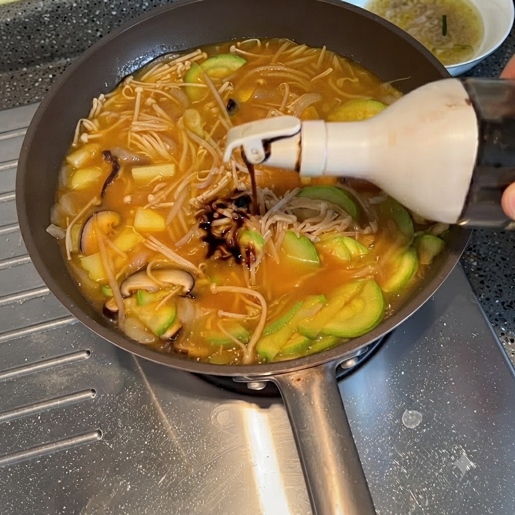 Sojasauce wird aus einer Flasche in den köchelnden Gemüseeintopf gedrückt.