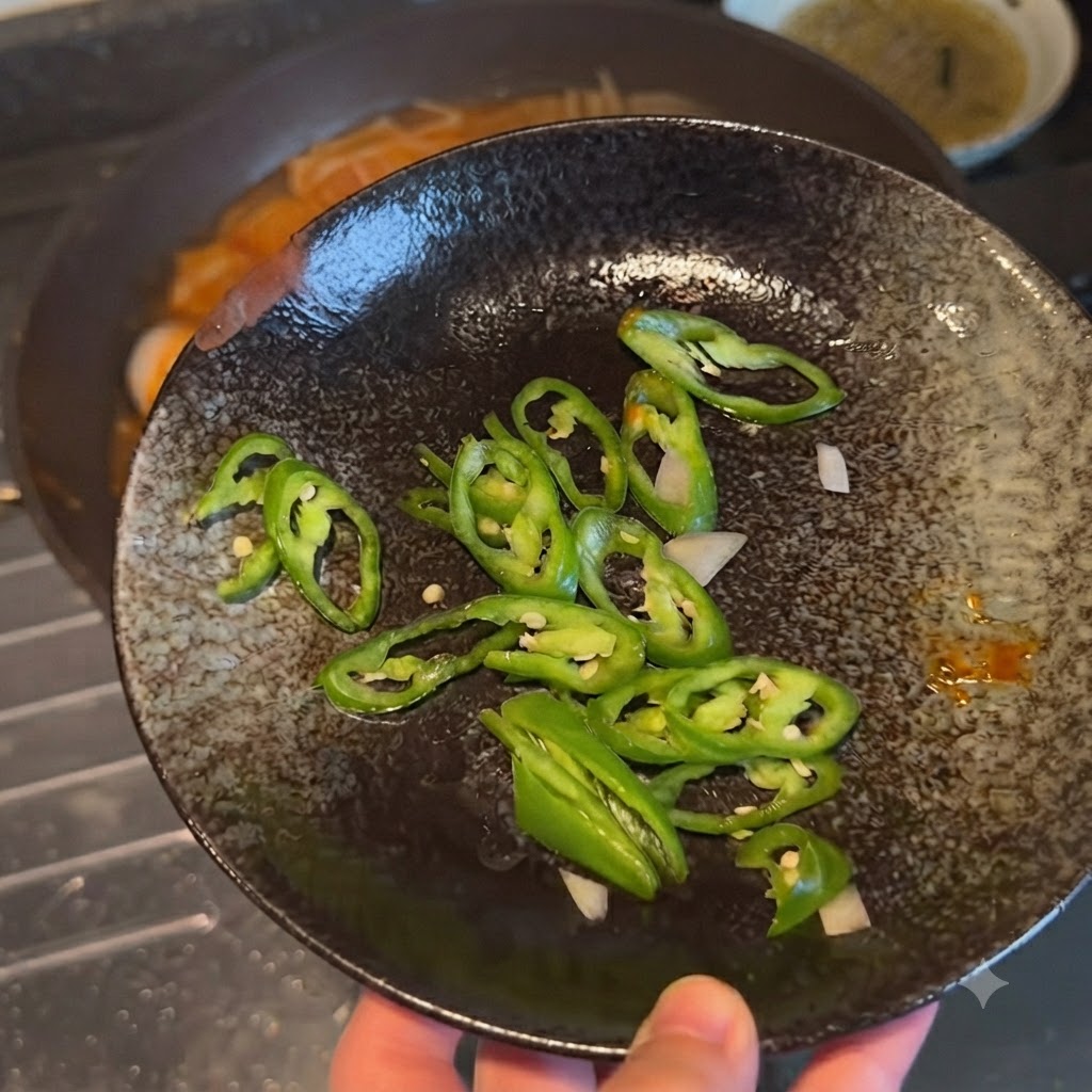 In Scheiben geschnittene grüne Chilischoten auf einem dunklen Deko-Teller, bevor sie zum Gericht gegeben werden.