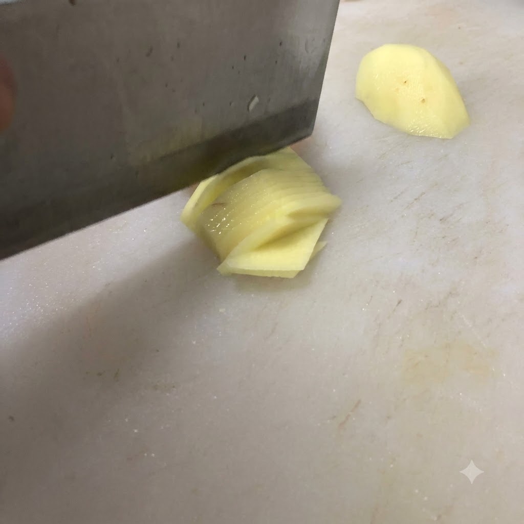 Ein Messer schneidet eine Kartoffel auf einem weißen Schneidebrett in dünne Stücke.