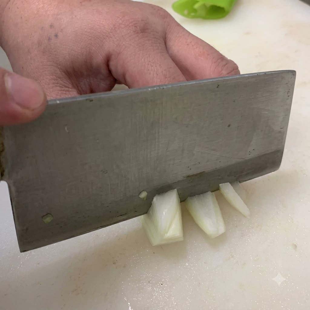 Ein Messer schneidet eine Zwiebel auf einem weißen Schneidebrett in Stücke.