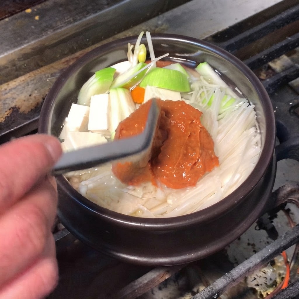Ein Silikonspatel gibt reichhaltige braune Sojabohnenpaste und rote Chilipaste in den Kochtopf.
