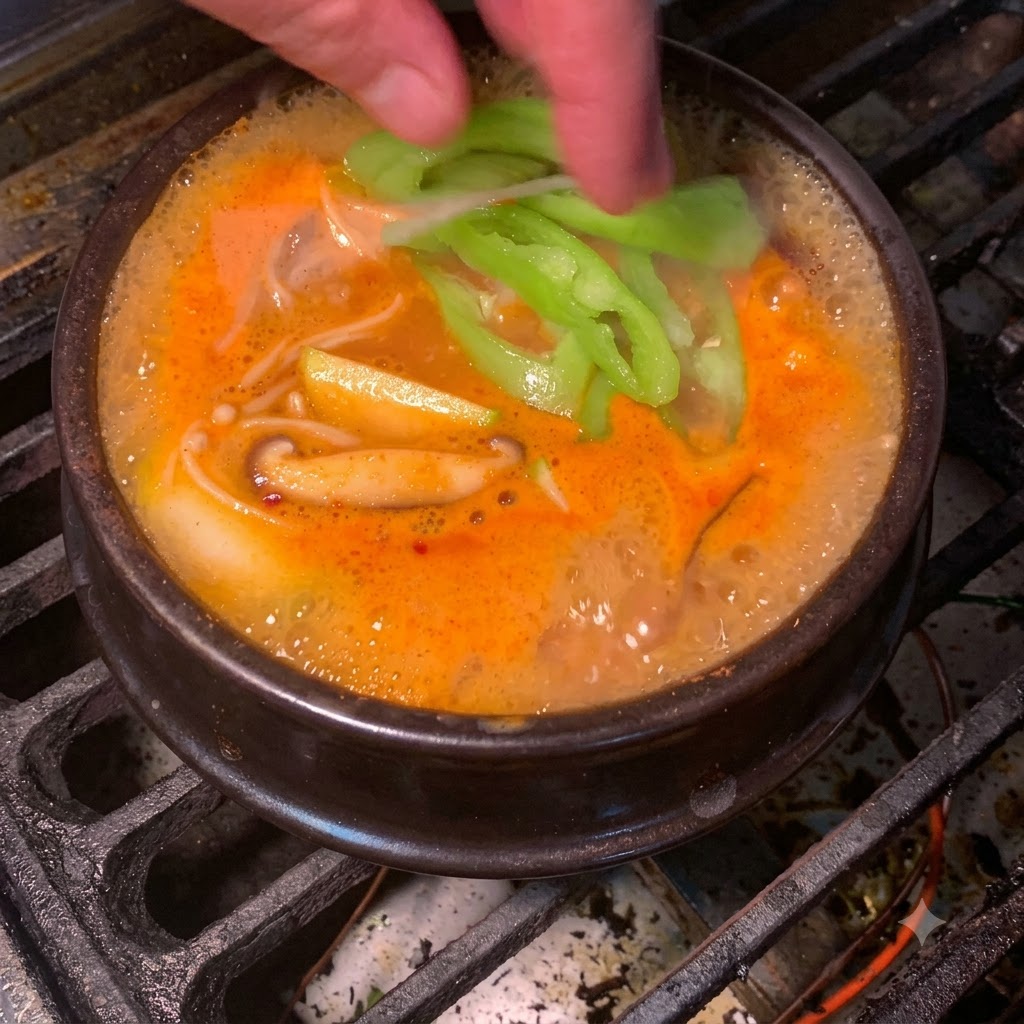 Frische grüne Chilischeiben werden in den blubbernden orange-roten koreanischen Sojabohnenpasten-Eintopf geworfen.