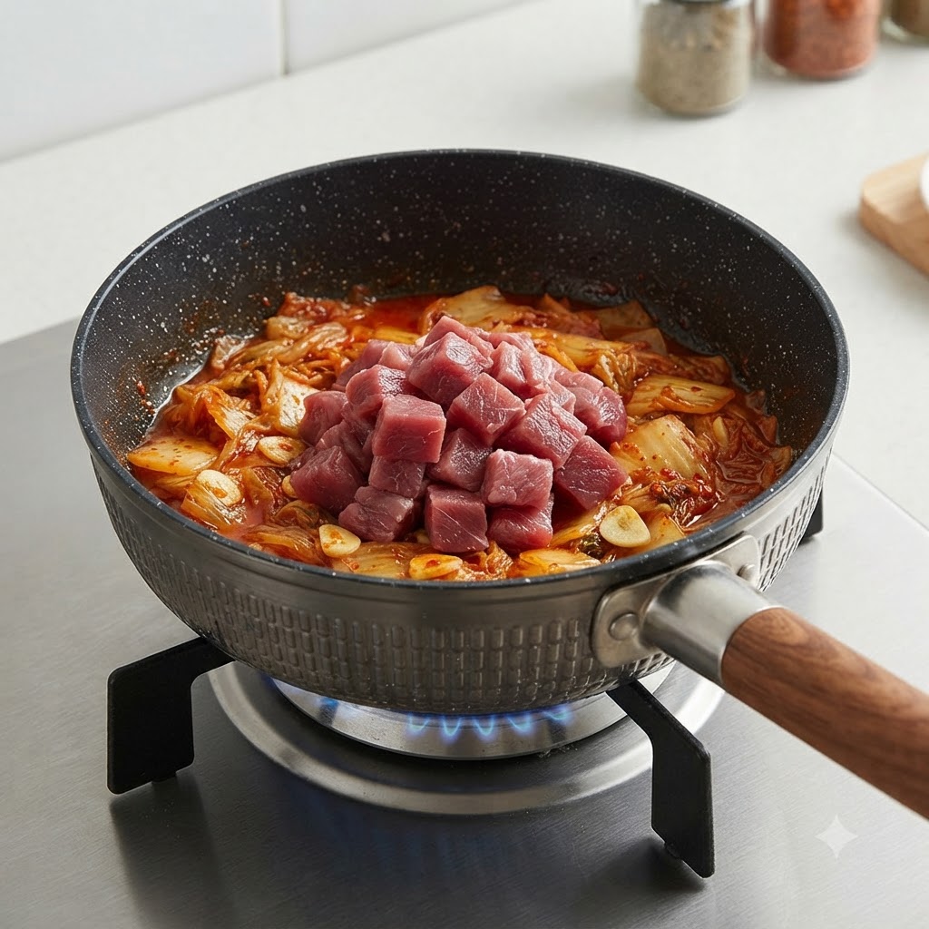 Rohe Rinderwürfel liegen oben auf dem angebratenen Kimchi in einem Topf.