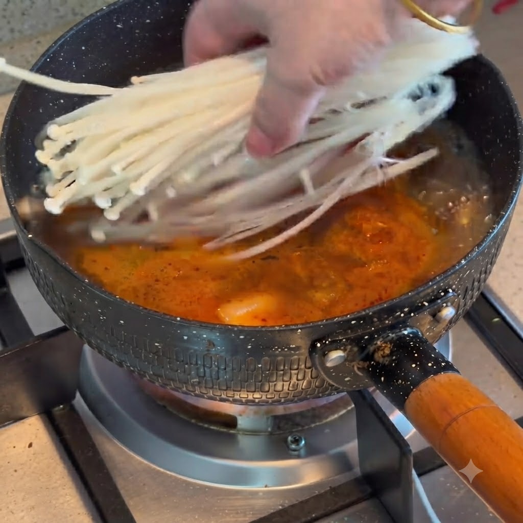 Enoki-Pilze werden in einen Topf mit kochendem Kimchi-Rindfleisch-Eintopf gegeben.