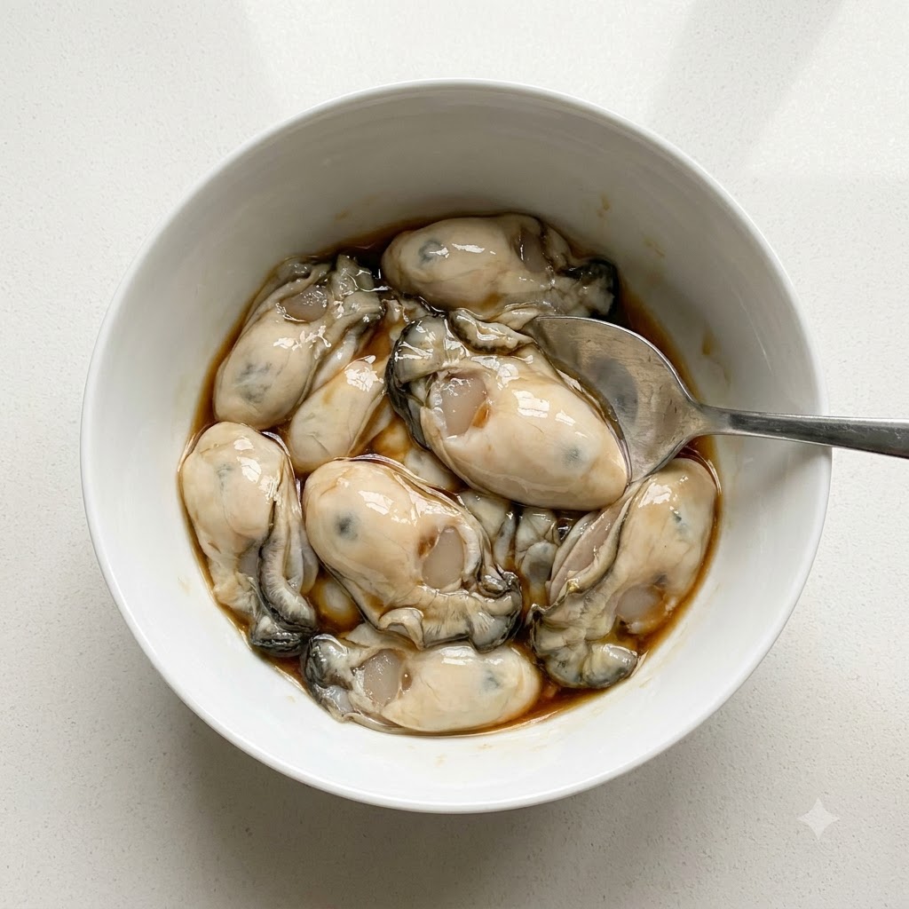 Gereinigte Austern in einer weißen Schüssel werden mit Fischsoße und weißem Pfeffer mit einem Löffel gewürzt.