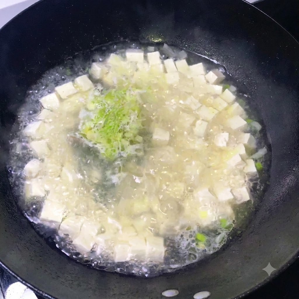 Gewürze werden über einen köchelnden Topf mit Tofu und gehackten Frühlingszwiebeln gestreut.