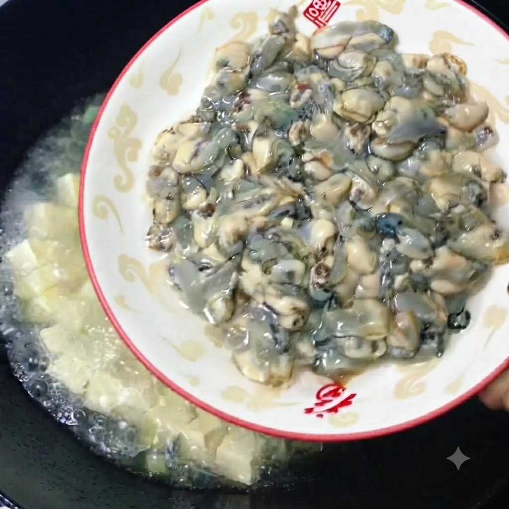 Frische, pralle rohe Austern werden von einem dekorativen Teller in einen Wok mit köchelnder Tofubrühe geschoben.