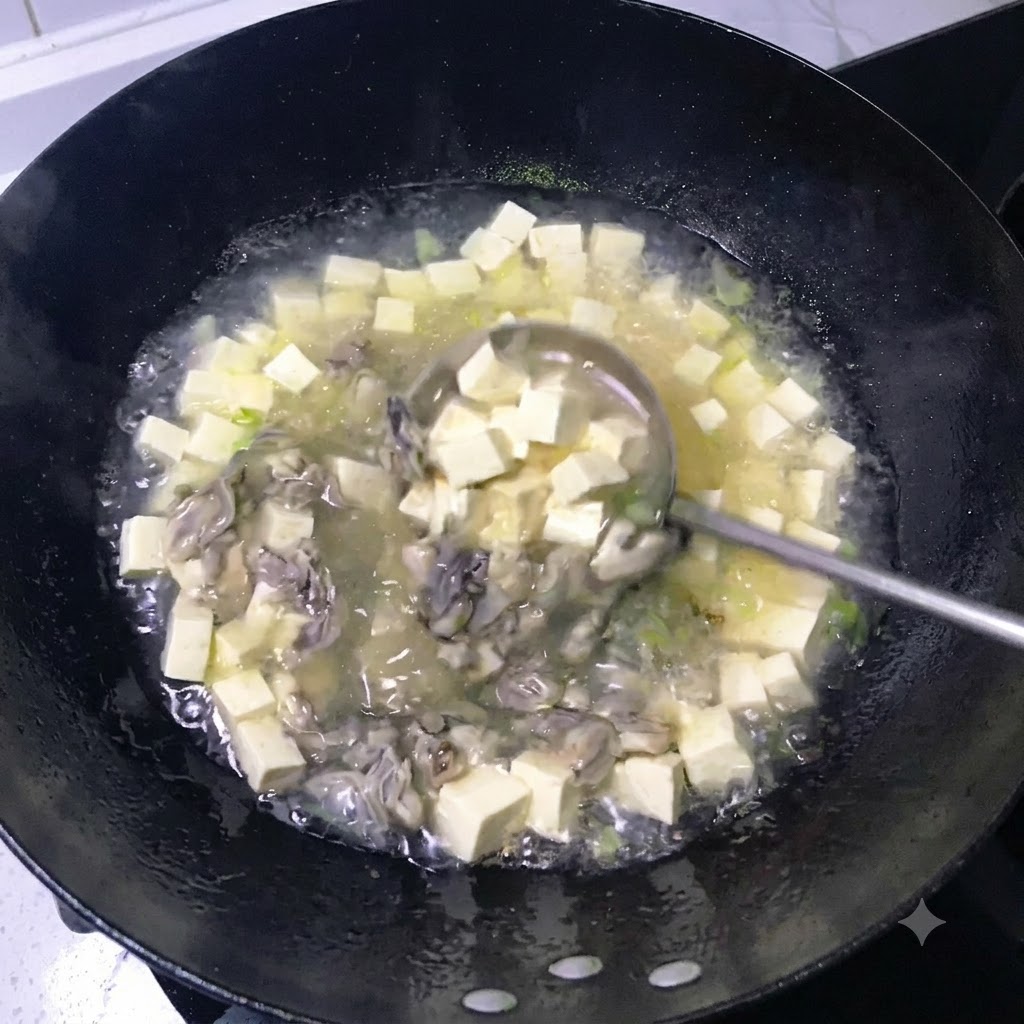 Eine Kelle rührt eine köchelnde, milchig-weiße Brühe voller gewürfelter Tofustücke und gekochter Austern in einem schwarzen Wok um.