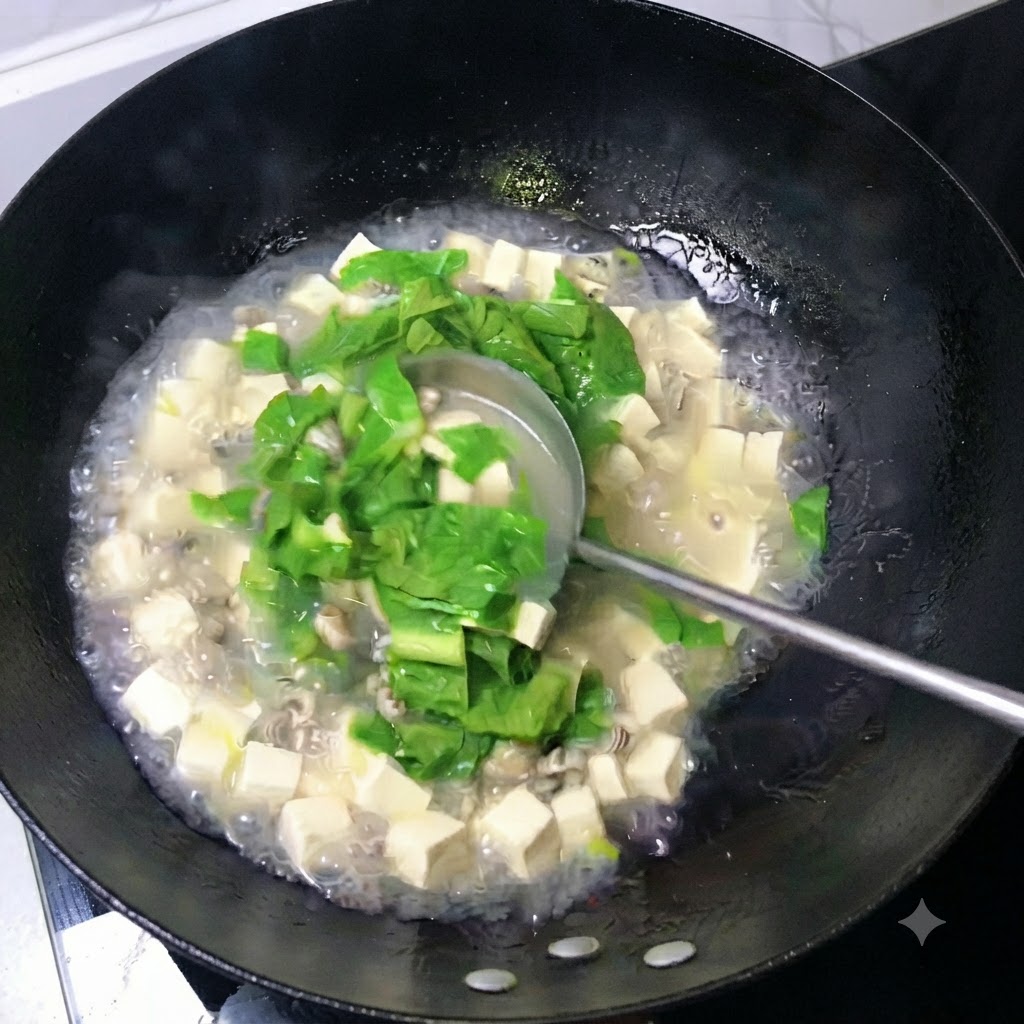 Eine Kelle rührt eine milchig-weiße Brühe mit Tofuwürfeln, Austern und grünen Blättern in einem Wok um.