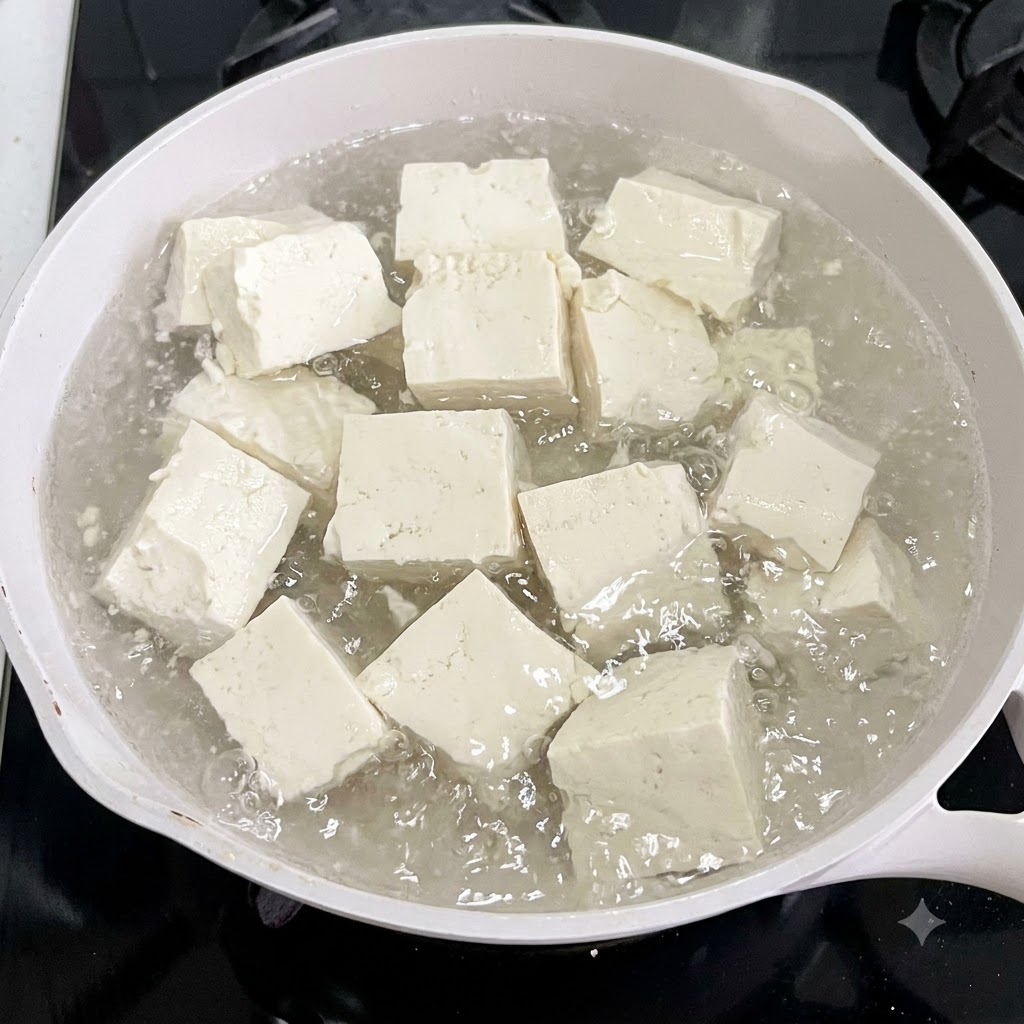 Tofuwürfel kochen in einem weißen Topf mit Wasser und Ingwerscheiben.