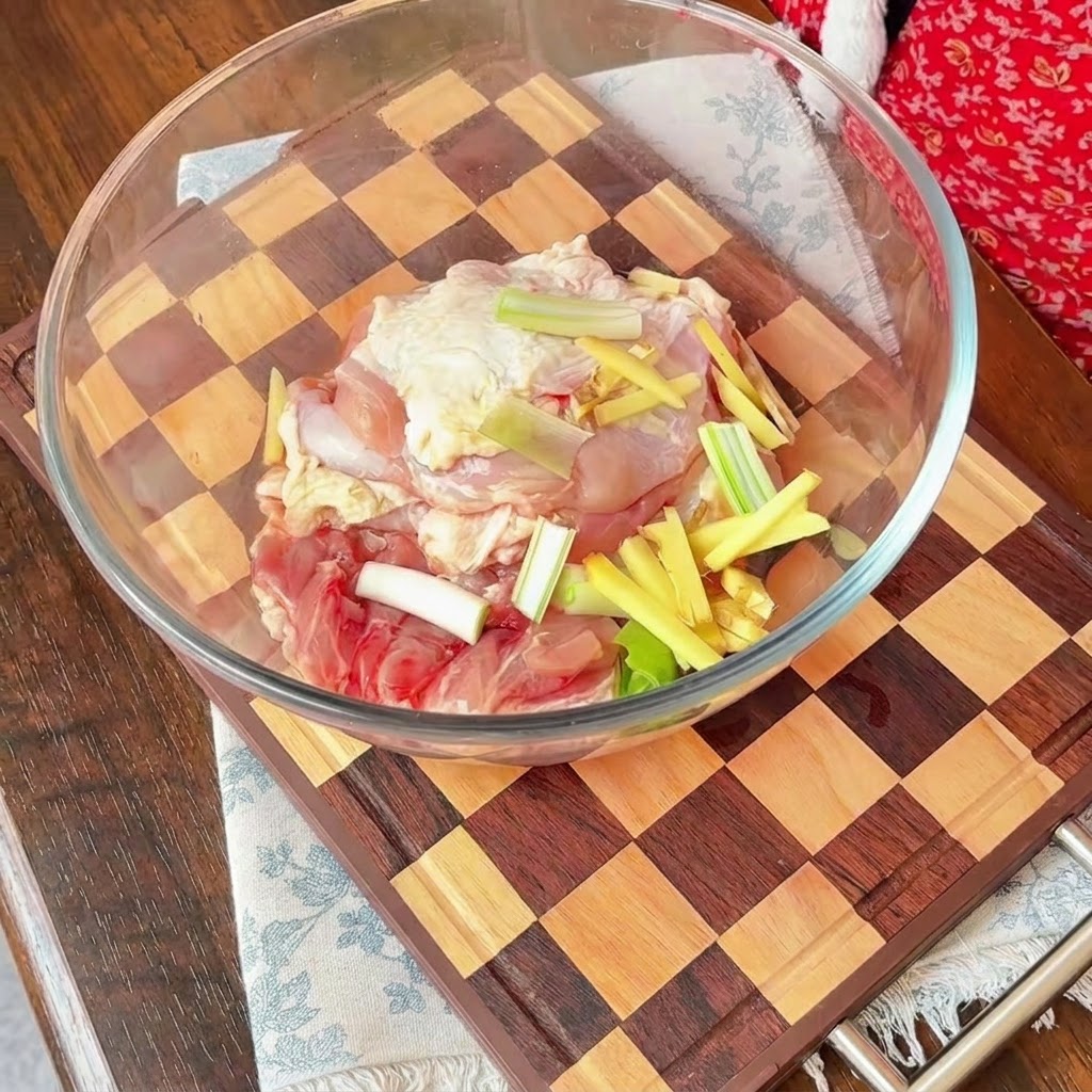 Rohe Hähnchenstücke in einer Glasschüssel mit roten Zwiebeln, Frühlingszwiebeln und Ingwerstreifen.