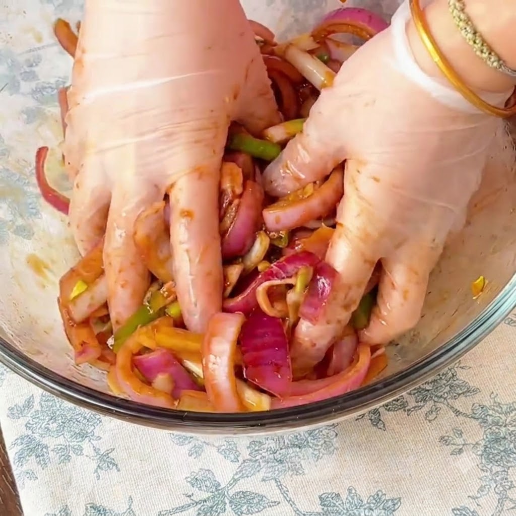 Hände massieren Marinade und Zwiebeln in das Hähnchen in einer Glasschüssel ein.
