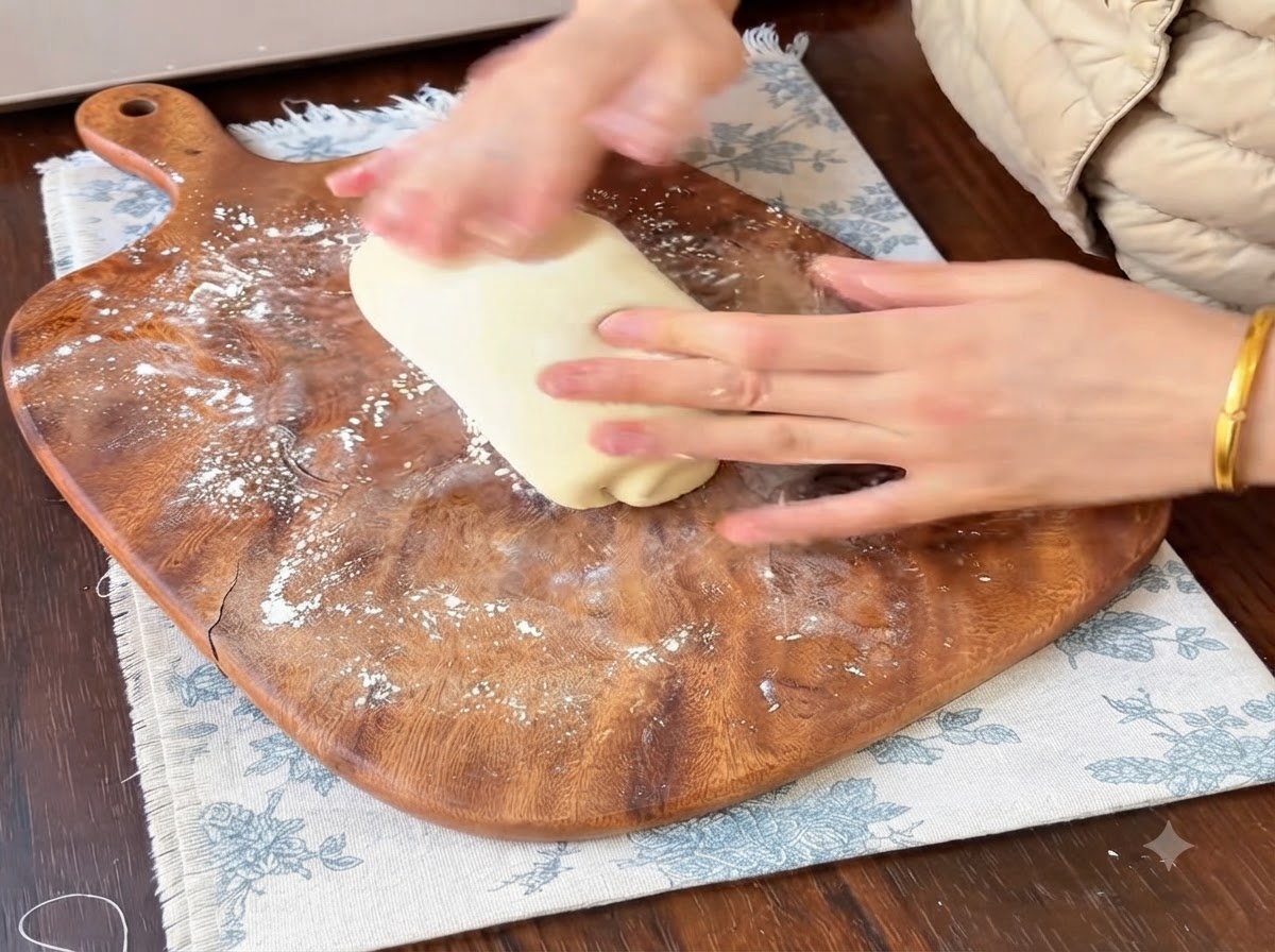 Hände rollen und formen Teigportionen auf einem bemehlten Holzschneidebrett.