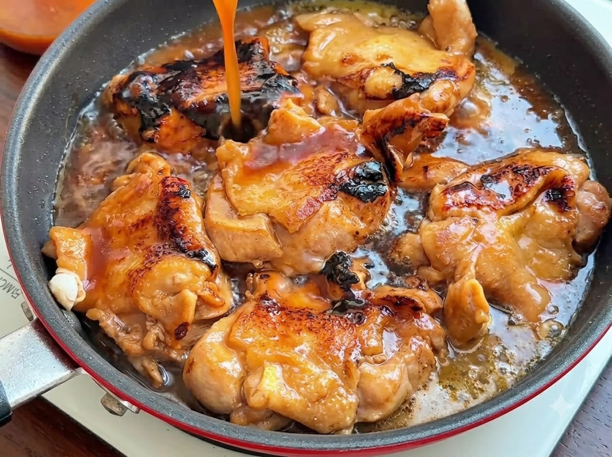 Dunkelbraune Sauce wird von oben in eine Pfanne mit gebratenen Hähnchenschenkeln gegossen.