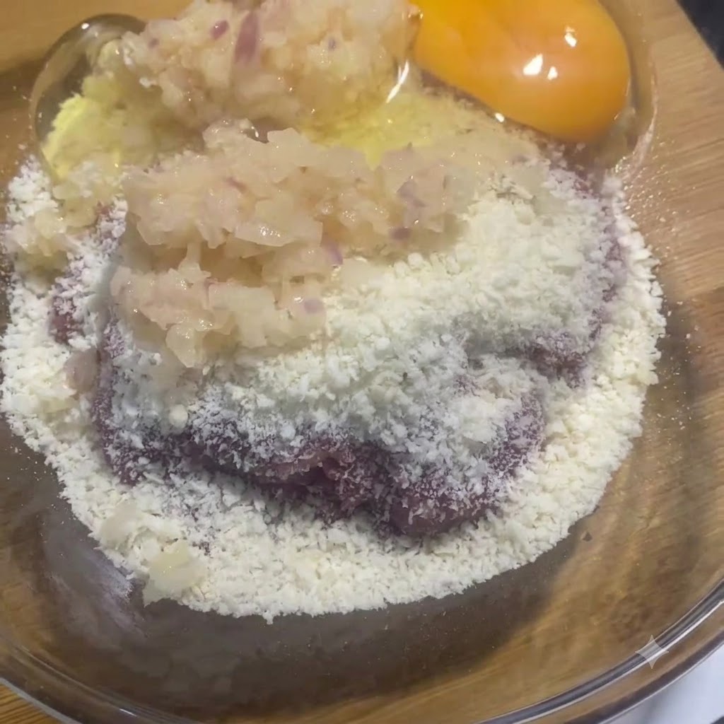 Ein rohes Eigelb und Eiweiß in der Glasschüssel neben der Fleisch- und Zwiebelmischung.