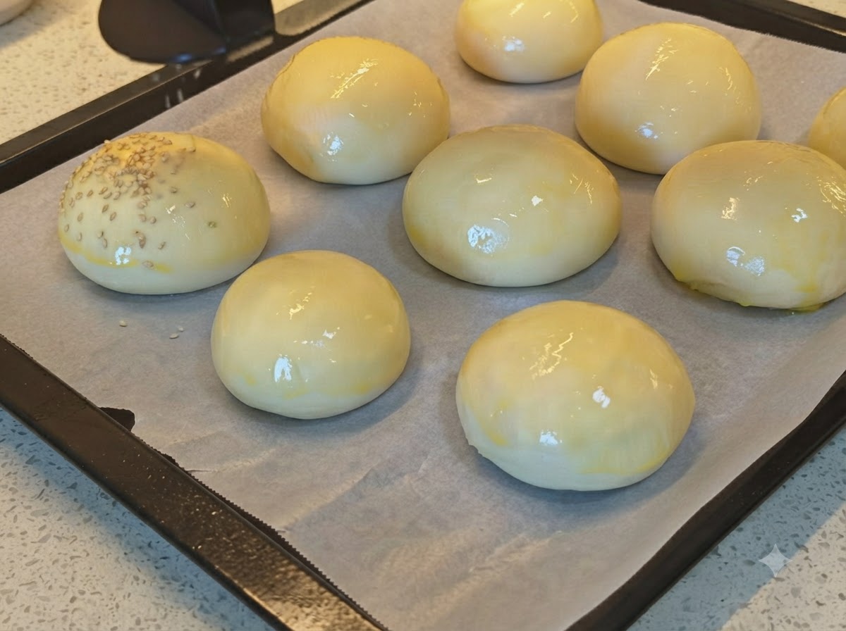Sesamsamen werden auf ein Blech mit glänzenden, mit Ei bestrichenen Brotbrötchen gestreut.
