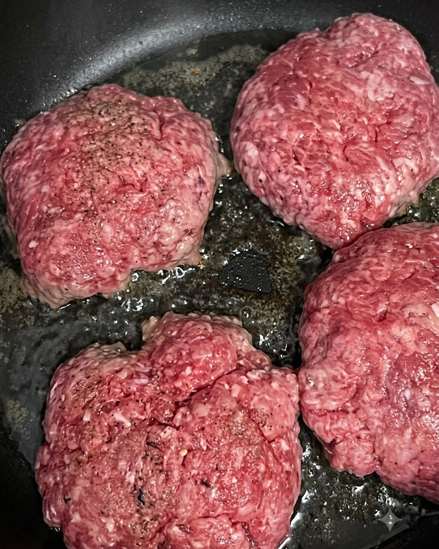 Vier rohe Rindfleisch-Patties brutzeln und bräunen in einer heißen Pfanne.